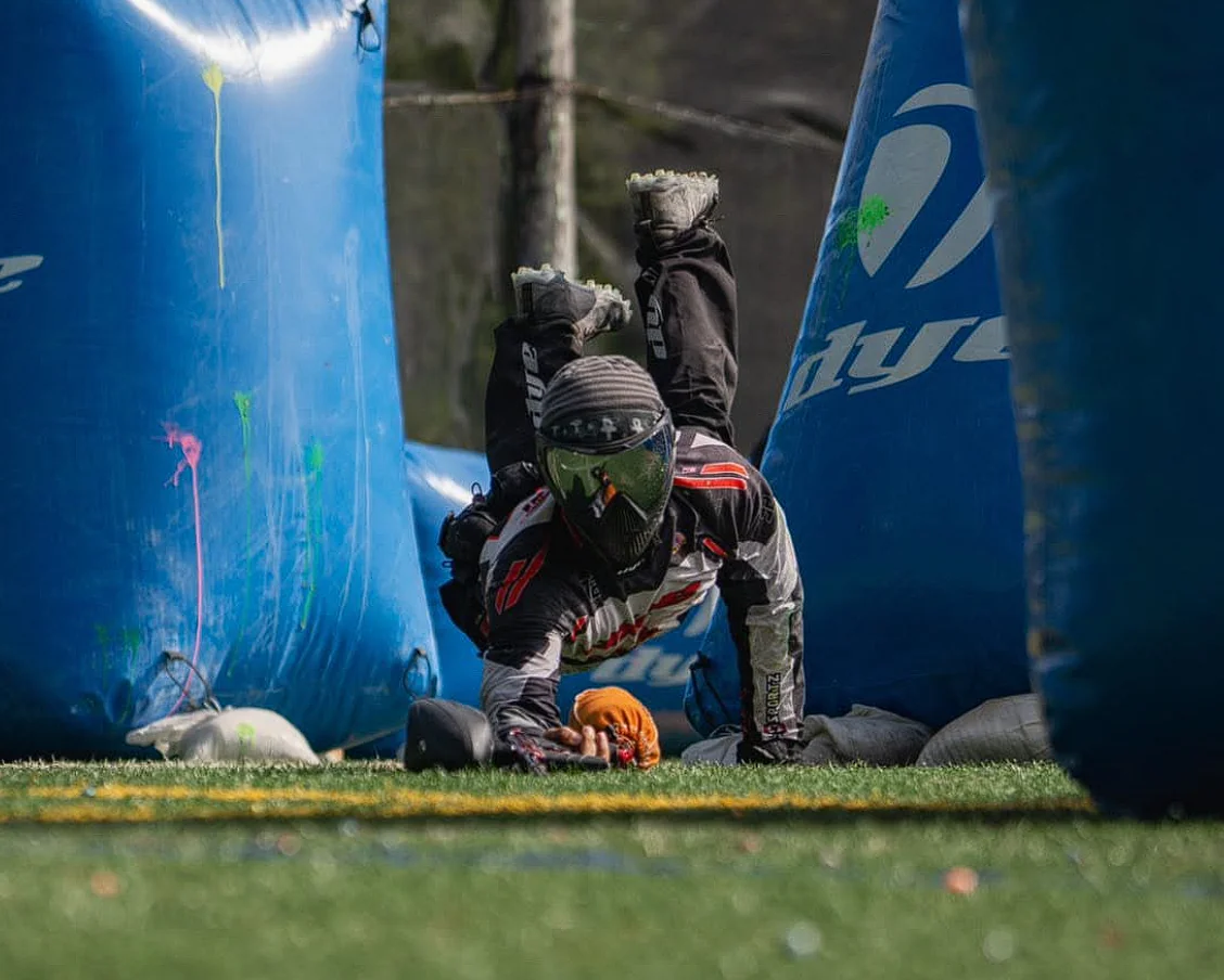 Masked paintball player diving between blue inflatable Speedball bunkers